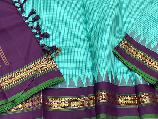Gopura Neelam — Kanchipuram Pure Silk Saree
 
 
Teal-green body with micro kattam checks for a sleek drape
Regal aubergine korvai border with gopuram/temple motifs & gold zari
Parrot-green selvedge for a fresh, festive pop of contrast
Aubergine pall