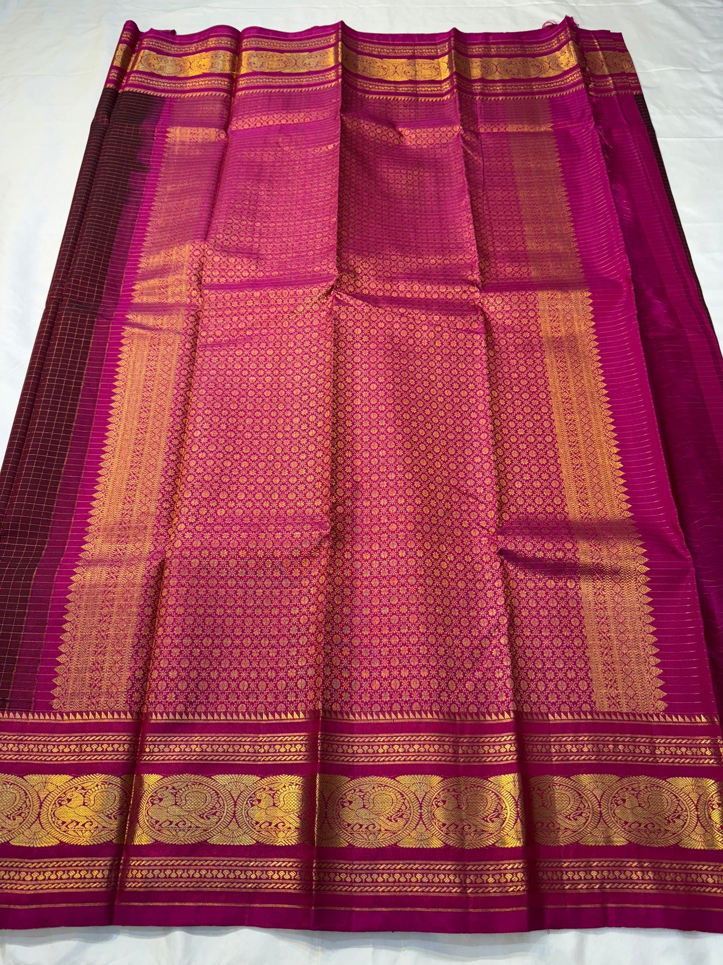 Arakku Kattam Mayura Chakram – Pure Silk Kanchipuram Saree (Maroon & Rani Pink)
Micro-check body with tiny gold buttas; vibrant rani contrast
Antique-gold peacock chakram border & grand woven zari pallu
Silk Mark Certified | Blouse Piece Included |