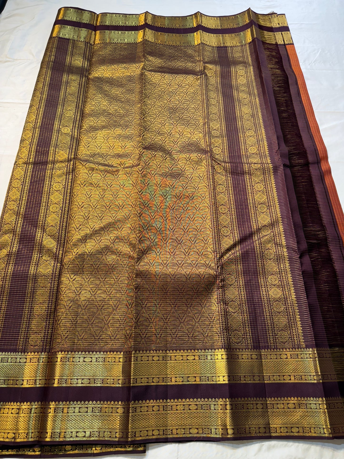 Rust Orange Kattam Rettapet – Pure Silk Kanchipuram Saree
Rust Orange Body with Petite Gold Buttas & Fine Kattam Grid
Deep Aubergine Rettapet Korvai Double-Line Contrast Border
Rich Zari Diamond & Chevron Brocade Pallu
Comes with Contrast Aubergine Blouse