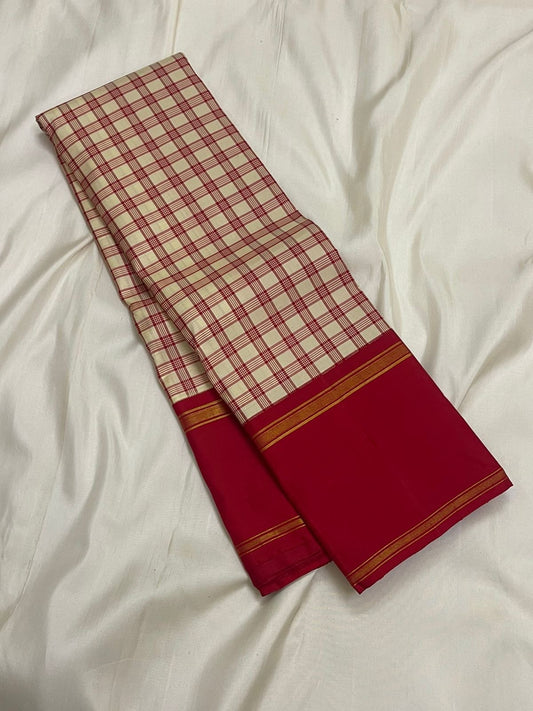 Cream silk saree with red kattam checks draped to show a deep red border finished with narrow gold zari woven stripes.