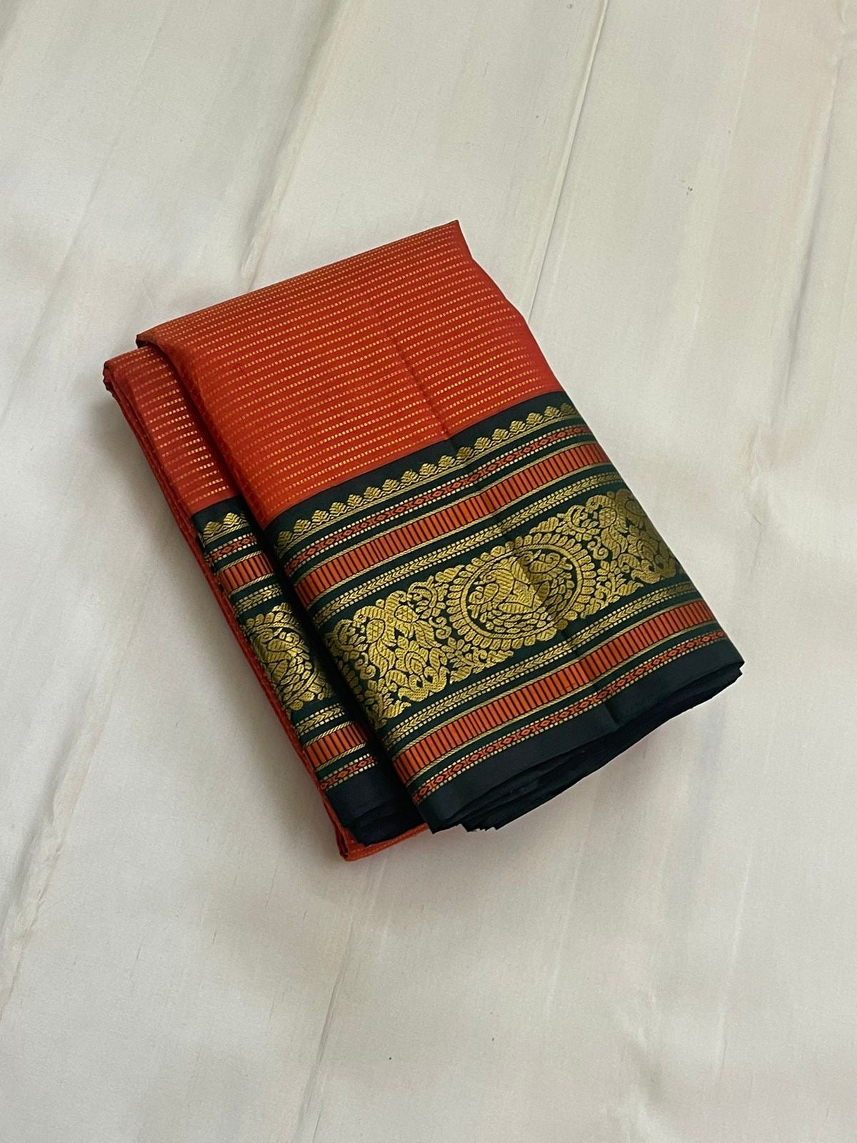 Aruna Mayil Chakram
Pure Kanchipuram Silk Saree – Reddish-Orange Body with Gold Zari Chakram Buttas
Contrast Bottle Green Korvai Borders with Mayil & Temple Motifs
Grand Zari Pallu with Diamond Brocade Weave & Hand-Knotted Tassels
Silk Mark Certified ✅ |