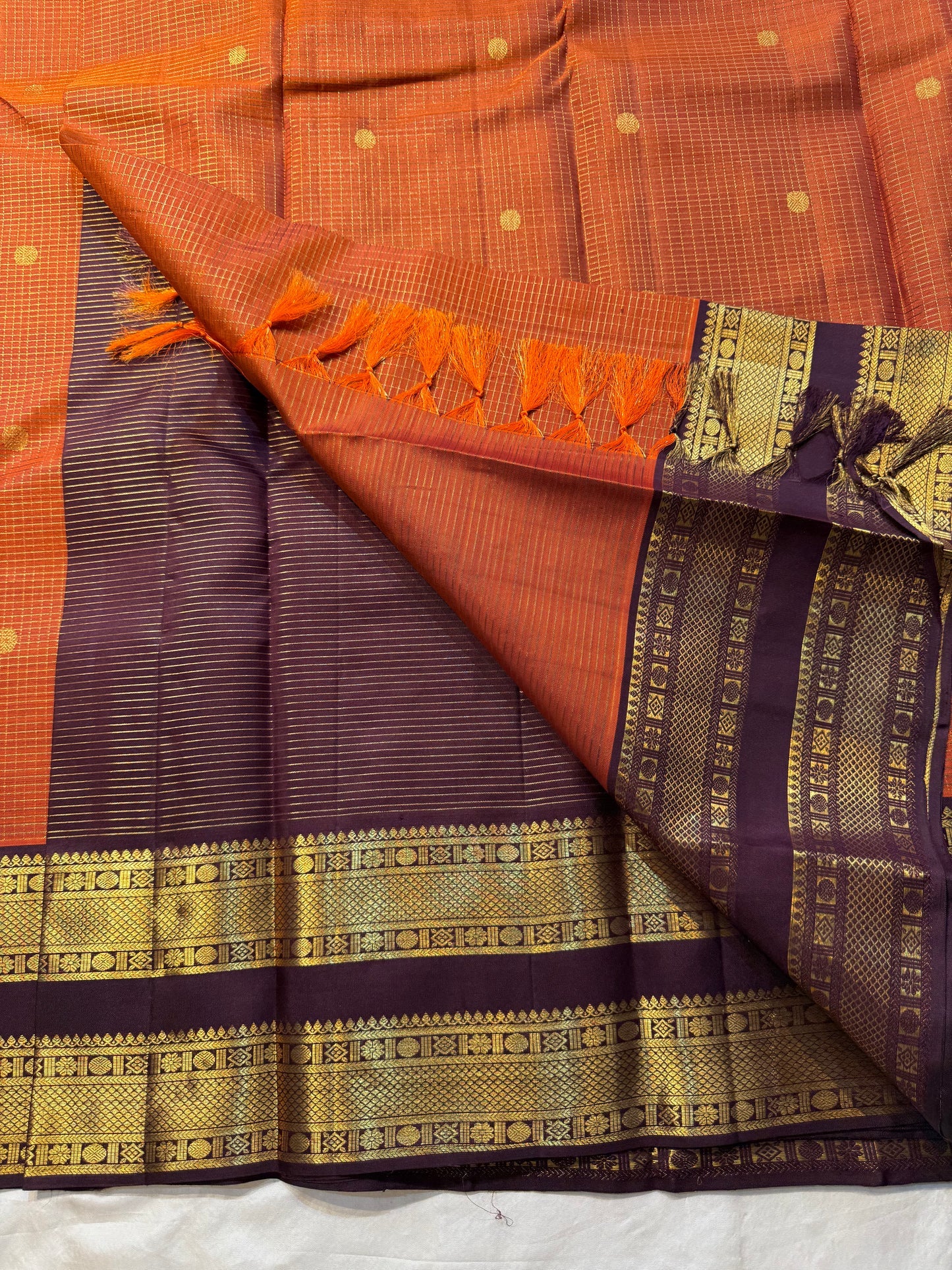 Rust Orange Kattam Rettapet – Pure Silk Kanchipuram Saree
Rust Orange Body with Petite Gold Buttas & Fine Kattam Grid
Deep Aubergine Rettapet Korvai Double-Line Contrast Border
Rich Zari Diamond & Chevron Brocade Pallu
Comes with Contrast Aubergine Blouse