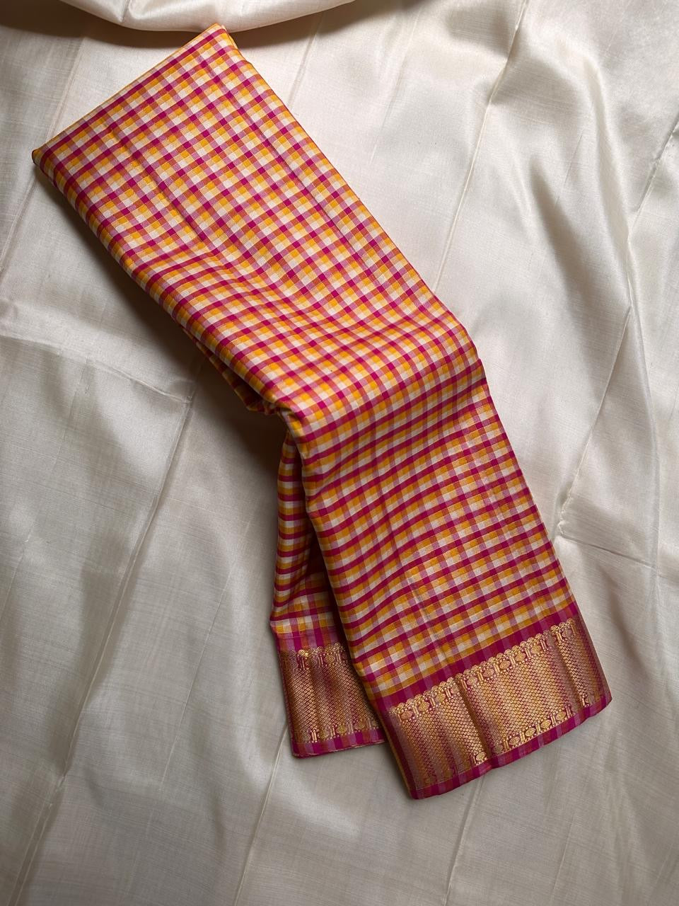 A classic Kanchipuram in Pattani Kattam checks with pink, magenta, mustard, and cream.
Finished with a contrast pink border and pallu.
Paisley and chakram motifs in a graceful grid add timeless charm.