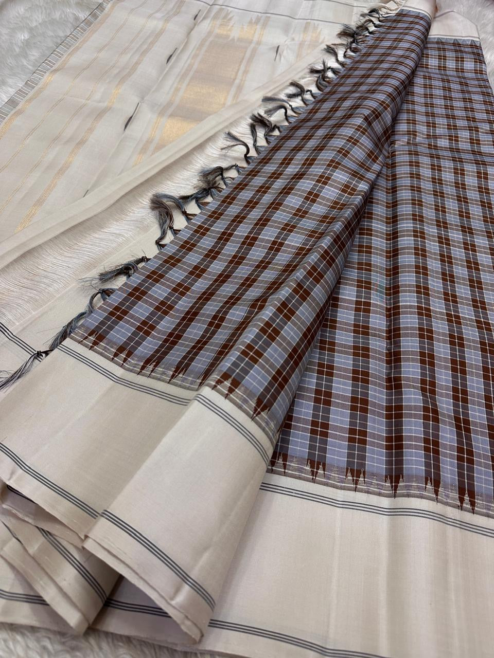 Nirai – Pure Kanchipuram Silk in Sandal, Grey & Mauve Checks.
Framed with a subtle sandal border and navy thread stripes, the saree features a striking pallu woven with thazhampoo reku and beautiful mullai mottu motifs in navy silk thread