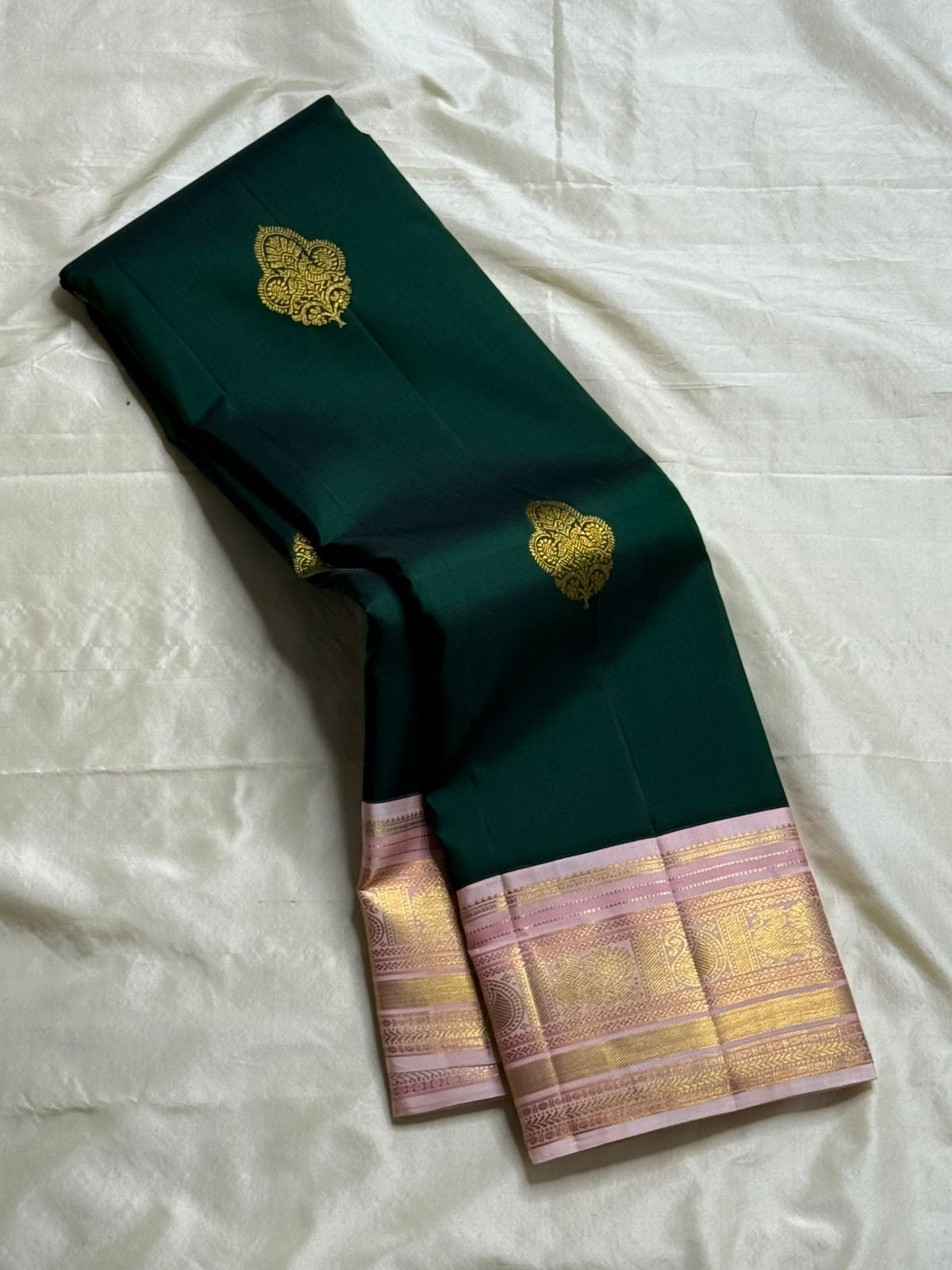 Rose-Tipped Emerald – Korvai Kanchipuram Pure Silk Saree
Emerald green body with zari paisley buttas
Blush-pink korvai border with muthuseer coin rows & vine motifs
Blush-pink zari-brocade pallu with elegant stripe details
Contrast blush blouse silk mark