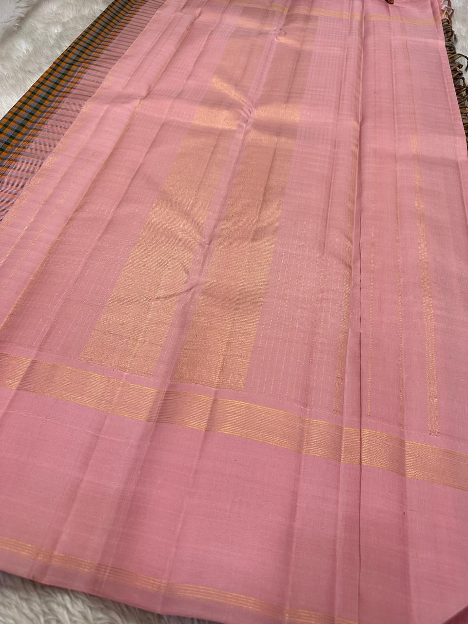 Nirai – A Madras-Inspired Kanchipuram Silk in Amber & Pastel Pink.
Woven with fine podi kattam checks in black, amber orange, and grey.
The pastel pink border with pillayar moggu detailing adds softness, with a seer zari pallu
