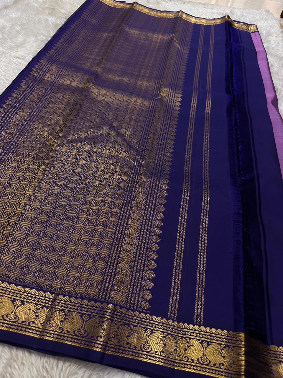 Lilac Mayil Pushpam – lilac-purple body with navy korvai borders
Pure Kanchipuram silk • gold zari pushpam (flower) buttas all over
Grand navy brocade pallu with diamond jaal • contrast blouse with border
Silk Mark Certified | Fall & Pico Done |