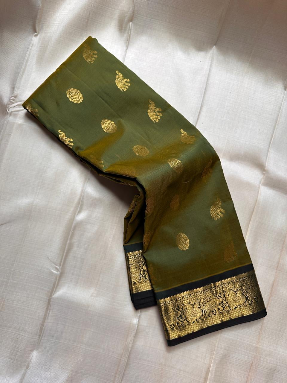 Olive Pachai – Pure Korvai Kanchipuram Silk Saree
Olive green body with gold zari gaja & medallion buttas
Contrast black korvai border with peacock & floral vines
Grand brocade pallu with lattice & temple patterns
Silk Mark Certified …chk description