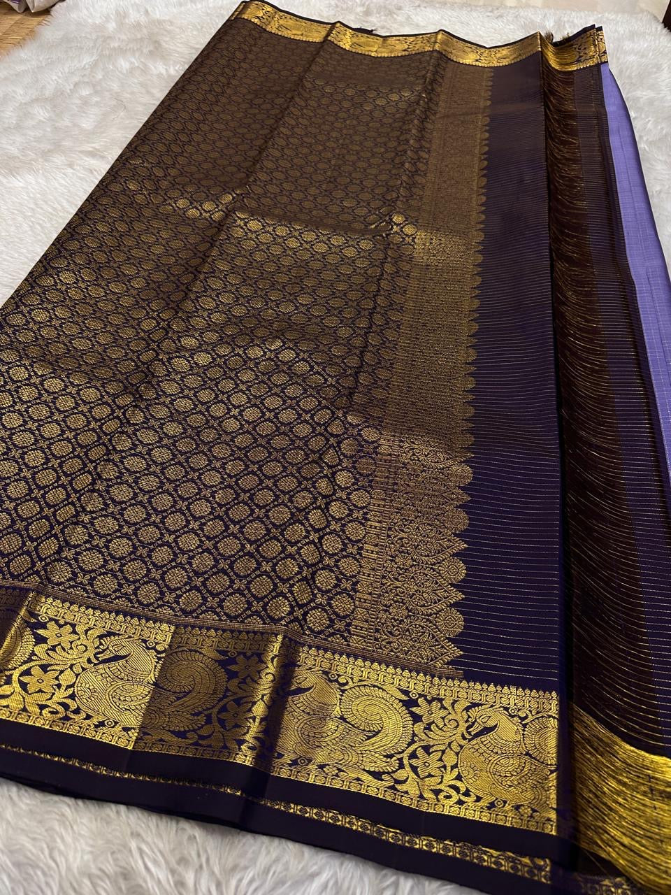 Classic heritage finesse in this lilac blue pure Kanchipuram silk saree Zari kattam , intricately handwoven with fine golden checks across the body. Scattered floral buttas add delicate charm,rich purple peacock border