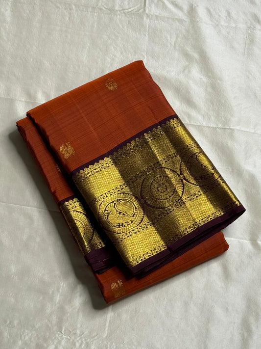 Rust Orange Supreme – Korvai Kanchipuram Pure Silk Saree
Shot rust-orange body with gold chakram & mankolam buttas all over
Deep purple korvai border with annam & chakram zari medallions
Rich vadamalli zari-brocade pallu | Contrast blouse | Fall & Pico Do