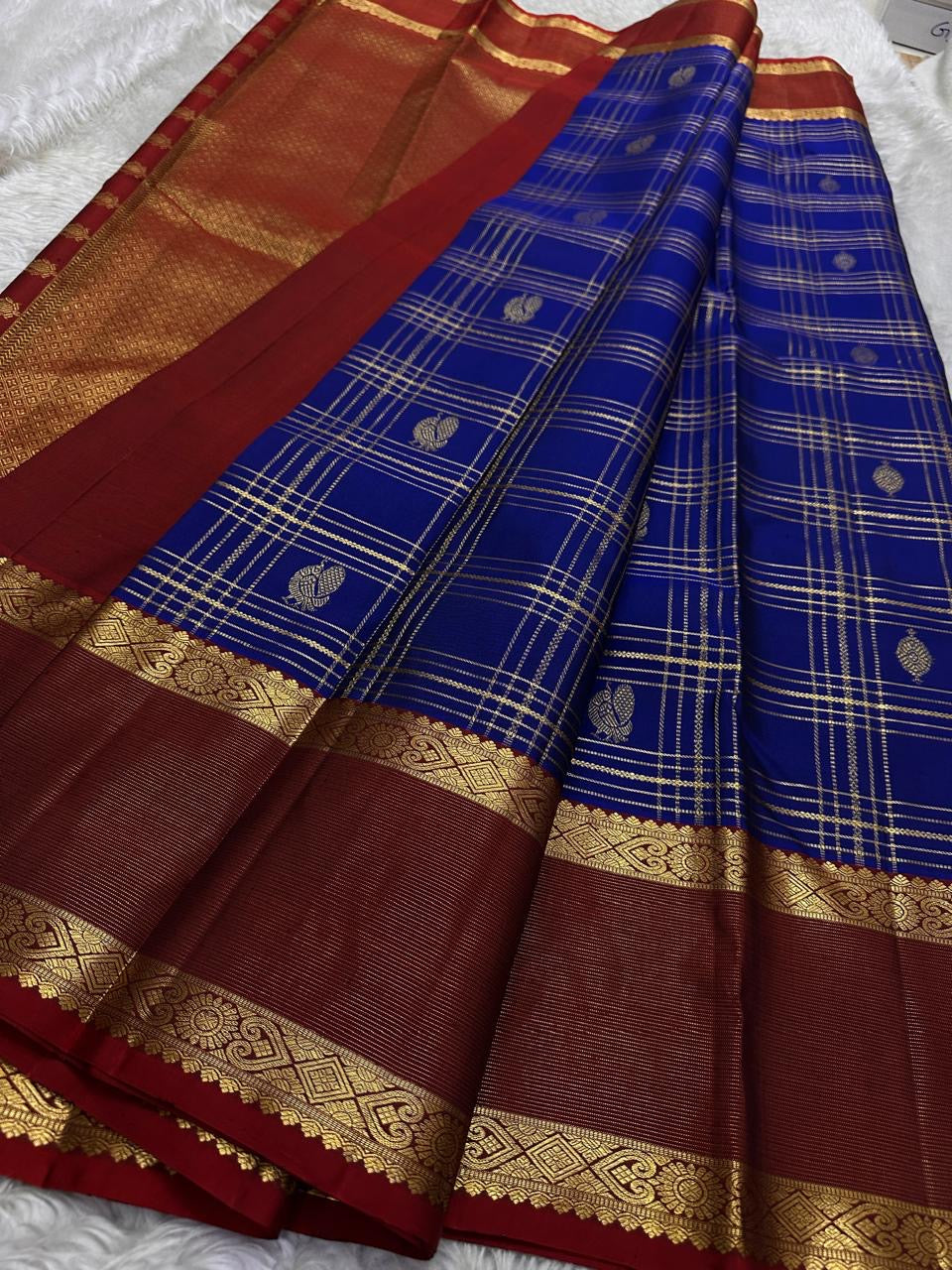 Sapphire Ruby Kattam – Pure Kanchipuram Silk Saree
sapphire blue body with gold kattam checks & buttas
Contrast ruby-red korvai borders with intricate gold zari weave
Grand ruby-red pallu with floral motifs
Silk Mark Certified | ships in 2 weeks