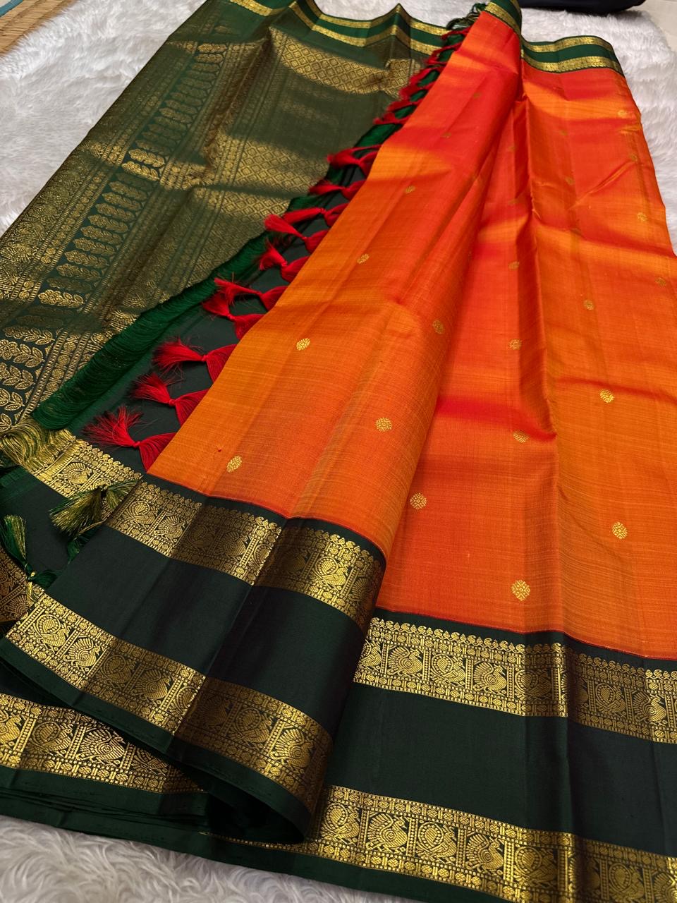 Riya – Orange Silk Saree with Dark Green Zari Border
Radiating warmth and festive charm, Riya glows in a rich ombré of orange and vermilion, adorned with dainty gold butta motifs that shimmer gently with movement.