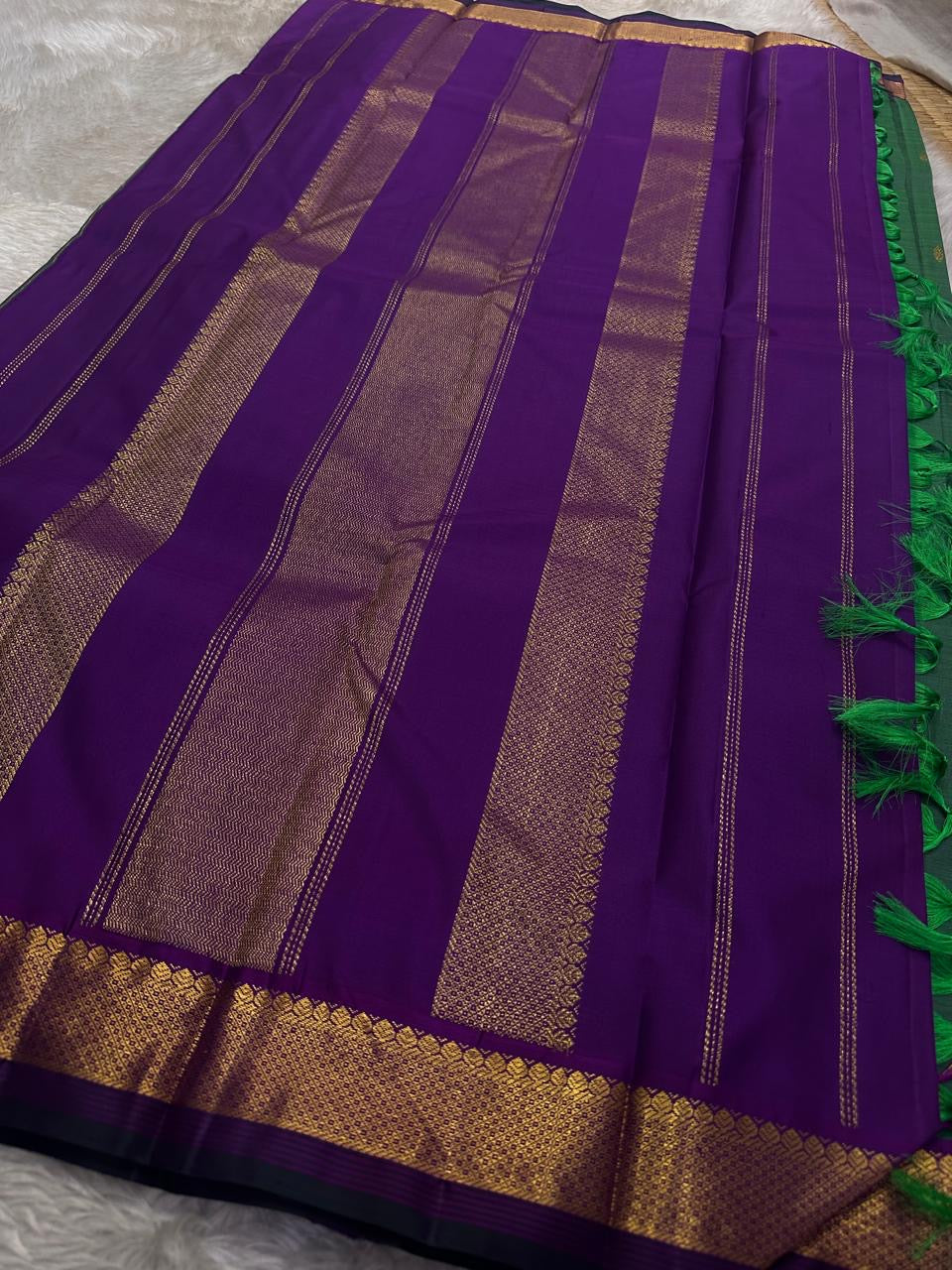 Varnam is a pure Kanchipuram silk saree in rich emerald green with subtle dual-tone shading. Woven gold zari buttas dot the body, while a petite purple border woven with intricate zari adds refined contrast. Arai maadam Pallu, jewel toned classic !