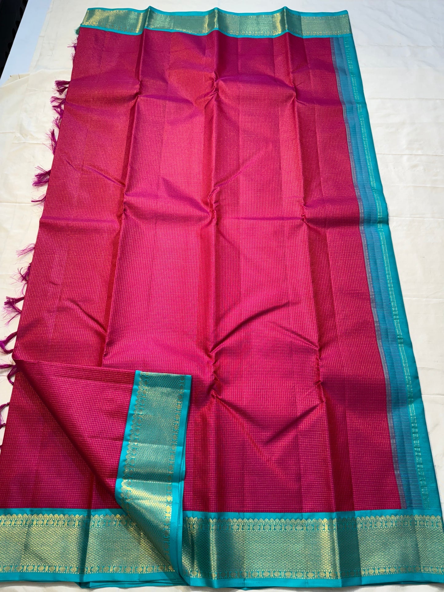 Leela Kattam — Kanchipuram Pure Silk
Rani-pink micro kattam body with soft vaira-oosi sheen
Contrast teal korvai borders with gold lattice & coin roundels
Rich teal pallu with all-over diamond/leaf zari jaal; rani tassels
Silk Mark Certified •