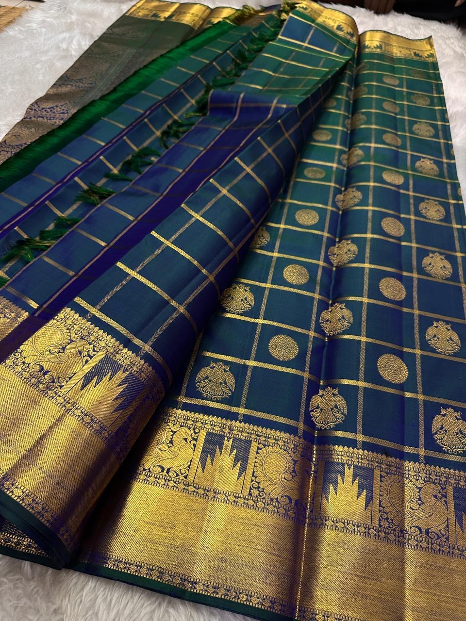 A celestial blend of blue and green, this Kanjivaram silk saree ,adorned with Gandaberunda and Kamalam buttas, golden checks, and a majestic thazhampoo Mayil border. Zari kattam