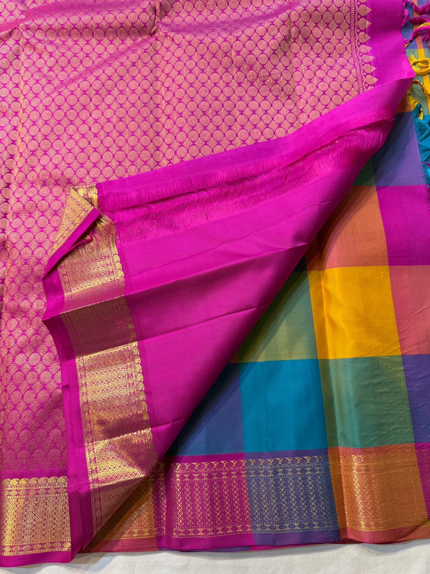 Rangoli Kattam – Pure Silk Kanchipuram Saree
Vibrant multicolor kattam checks with golden zari buttas across the body
Rich rani pink pallu with intricate zari weaving for a grand finish
Contrast purple borders edged with gleaming zari motifs