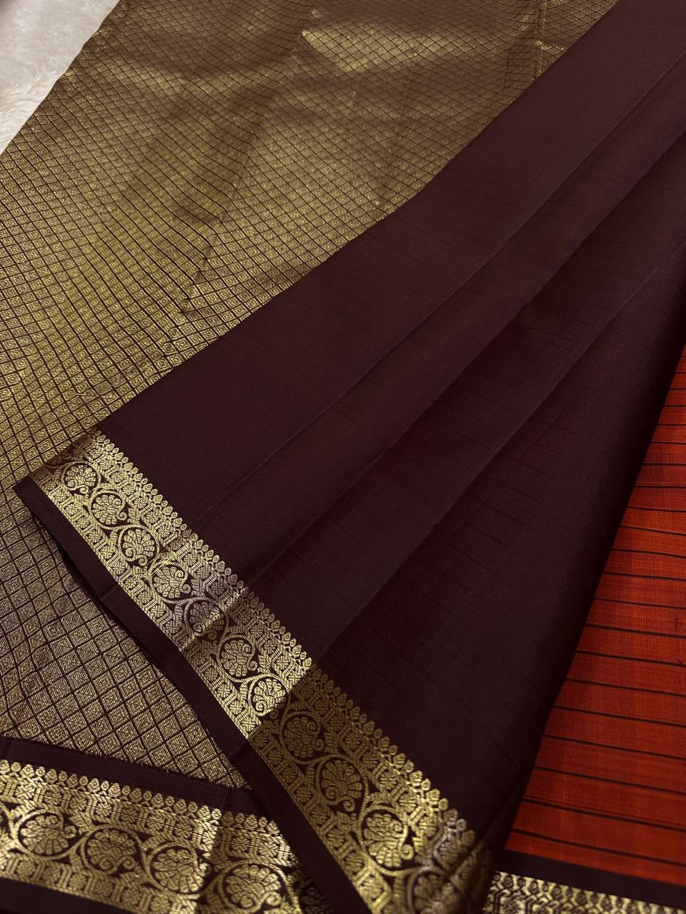 Terracotta Temple – Pure Kanchipuram Silk Saree
Brick red body with fine zari grid checks & golden buttas ✨
Deep coffee-maroon borders and grand diamond-jaal pallu in antique gold.