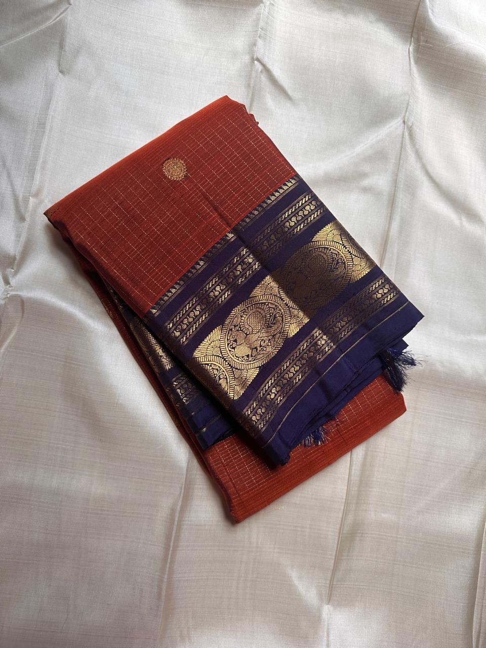 Rust Orange Neelam – Korvai Kanchipuram Silk Saree
Pure handloom silk | Rust-orange micro checks with gold chakram buttas
Neelam korvai border with annam chakram motifs & temple stripes
Grand zari-brocade neelam pallu | Contrast blouse | Fall & Pico Do