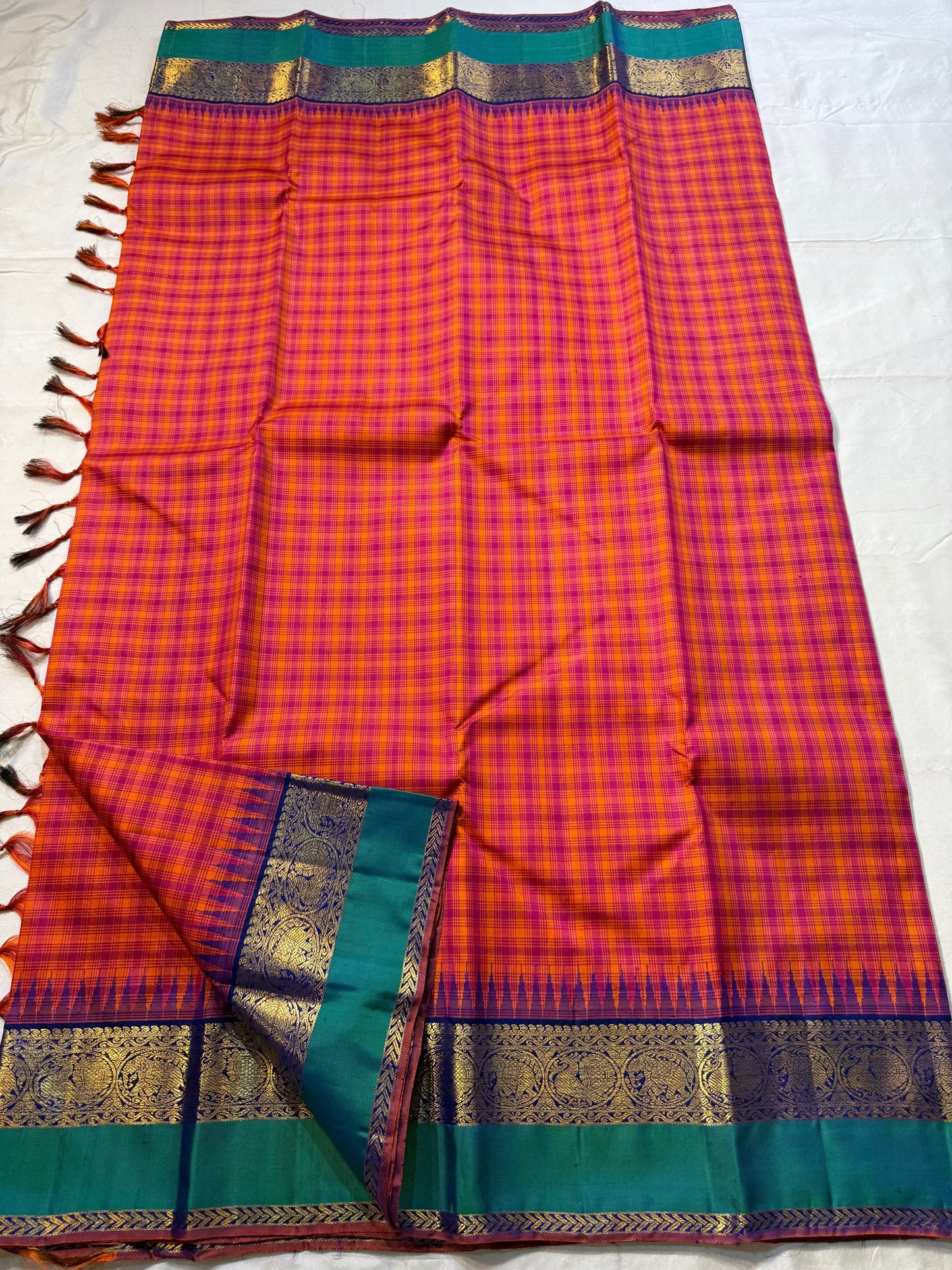 Chemman Maragatha Kattam
Pure Kanchipuram Silk Saree – Reddish-Orange & Maragatha Green Micro Checks
Deep violet korvai borders with gold zari floral motifs
Grand zari pallu with classic brocade detailing
Silk mark certified, ships in 2 weeks