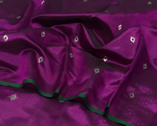 Draped in deep violet and plum, this pure silk Chanderi saree glows with a gentle sheen and graceful vertical zari lines. Delicate diamond meenakari motifs and finely woven borders lend a touch of tradition, with a contrast green selvedge