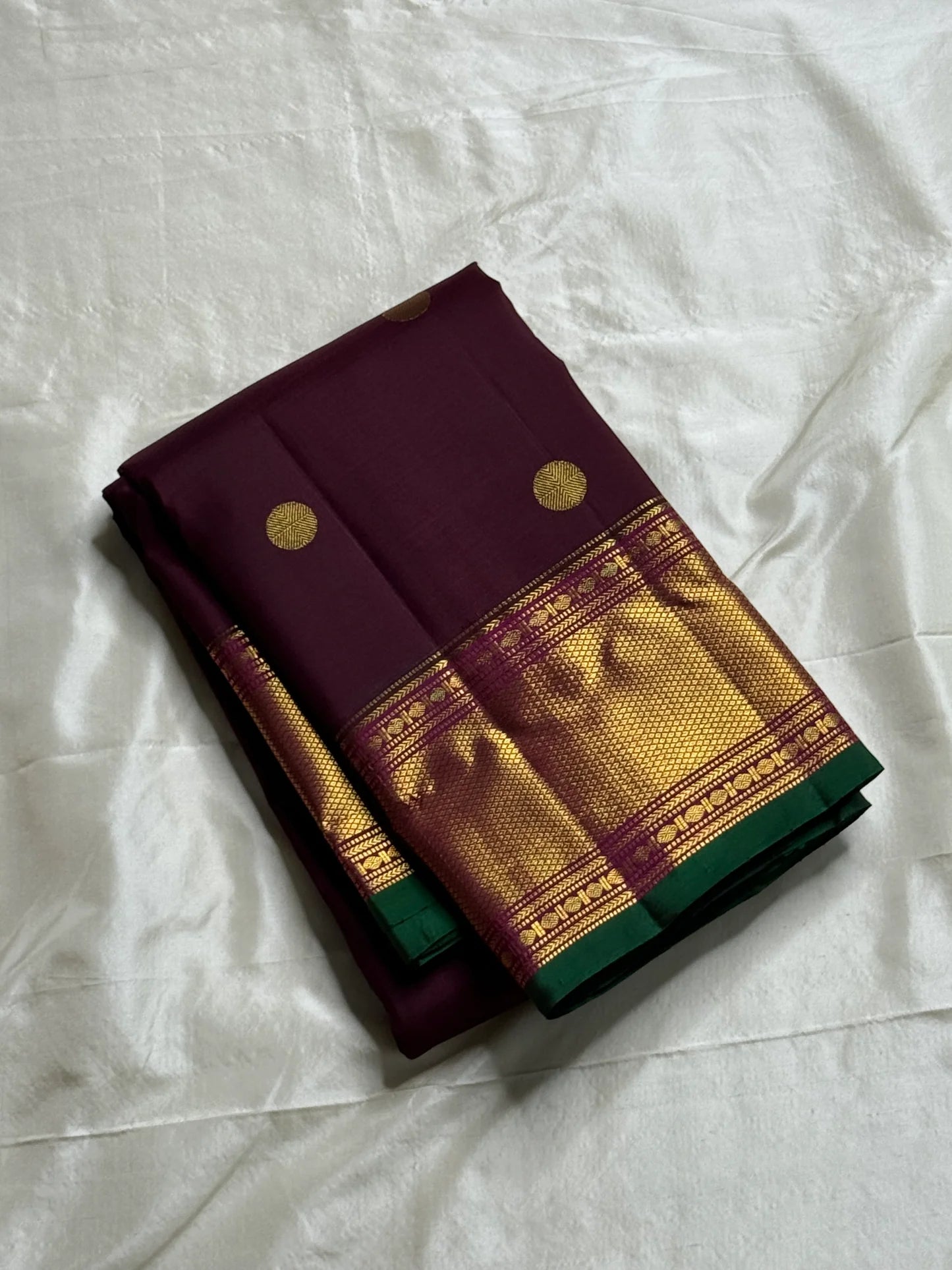 Plum & Magenta Round Butta – Pure Kanchipuram Silk Saree
Deep plum body with bold round gold zari buttas
Contrast green selvedge & gold tissue borders with magenta detailing
Grand magenta-pink pallu with full zari diamond jaal & geometric panels
Silk Mark