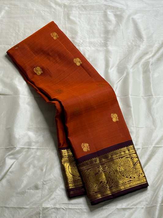 Rust Orange & Wine Korvai – Pure Kanchipuram Silk Saree
Burnt rust-orange shot body with dainty gold paisley buttas
Deep wine korvai borders in antique gold—Annapakshi & Yaali medallions
Grand wine pallu with full-zari jaal & temple panels
Silk Mark