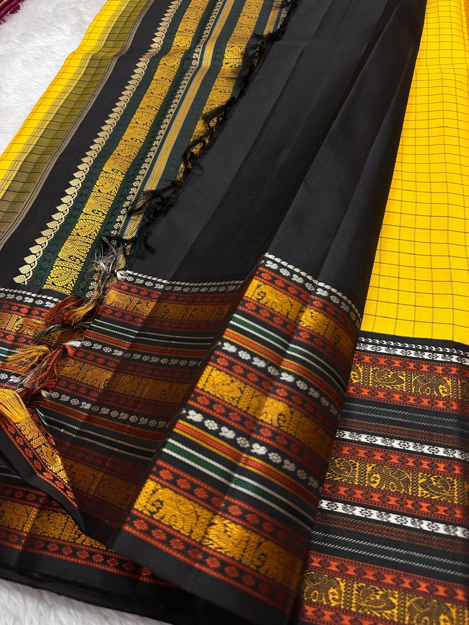 Marigold Mani Kattam – Pure Kanchipuram Silk Saree
Vibrant marigold yellow body with classic kattam checks
black borders with elephant & floral zari motifs
Rich black pallu adorned with green & zari stripes . Silk Mark Certified, delivery in 2 weeks