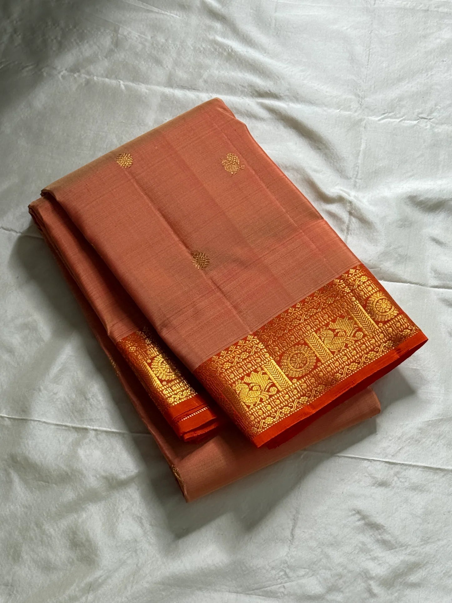 Mandara Peach – Pure Korvai Kanchipuram Silk Saree
Soft peach shot body with dainty gold chakram buttas
Vermilion-orange korvai borders with peacock medallions
Grand kumkumam red pallu with full zari brocade & temple panels
Silk Mark Certified | Free Ship