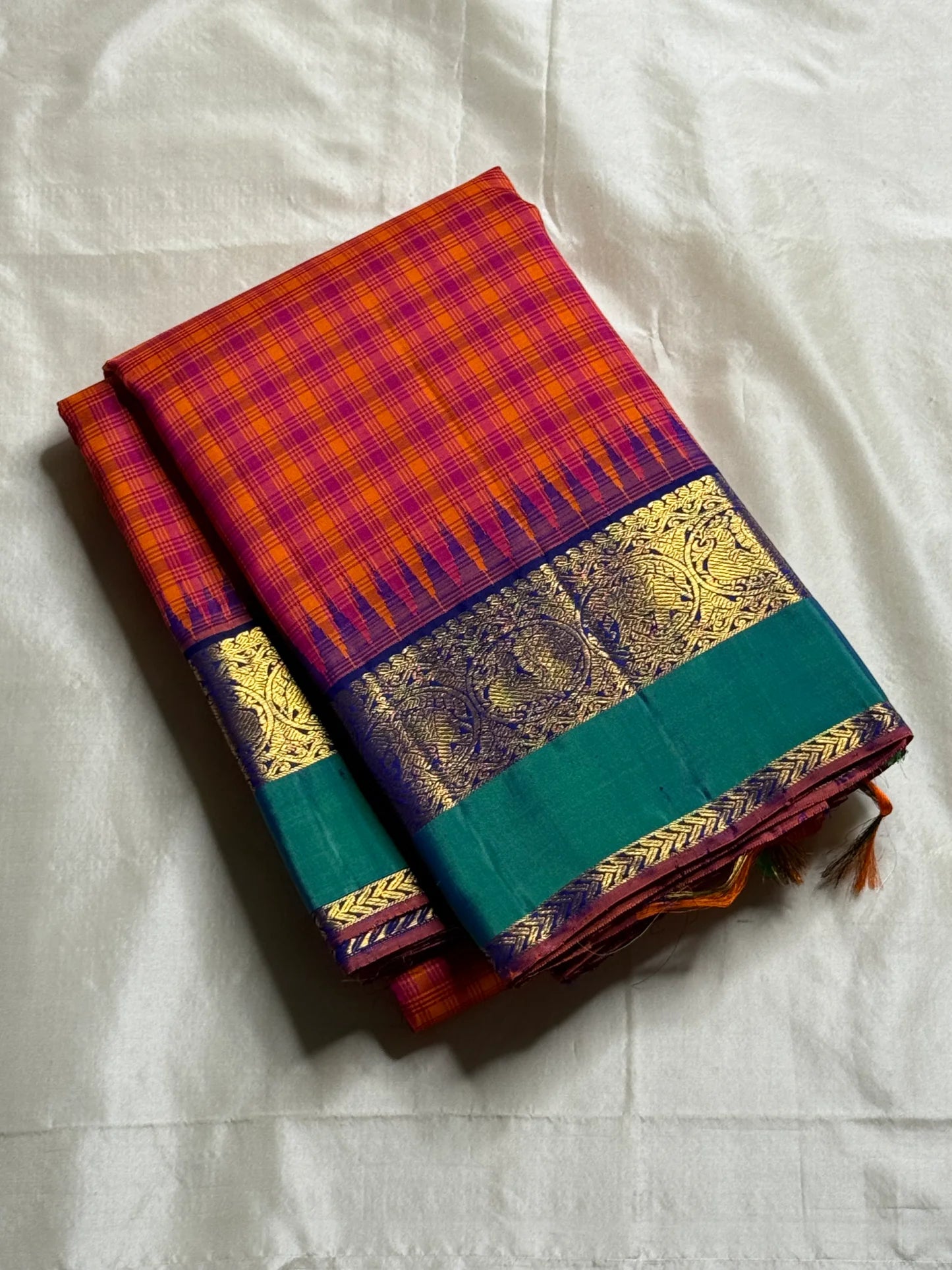 Chemman Maragatha Kattam
Pure Kanchipuram Silk Saree – Reddish-Orange & Maragatha Green Micro Checks
Deep violet korvai borders with gold zari floral motifs
Grand zari pallu with classic brocade detailing
Silk mark certified, ships in 2 weeks