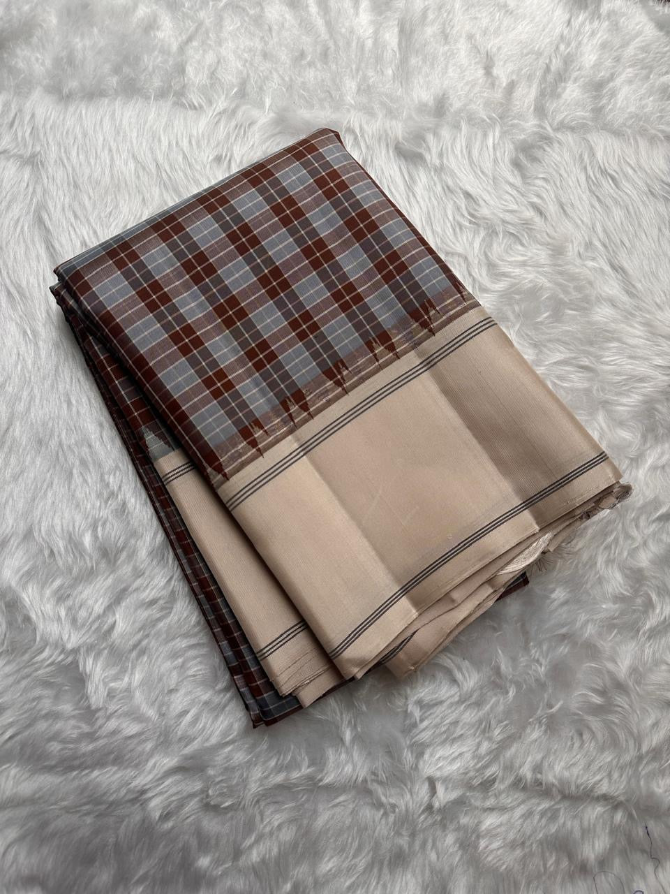 Nirai – Pure Kanchipuram Silk in Sandal, Grey & Mauve Checks.
Framed with a subtle sandal border and navy thread stripes, the saree features a striking pallu woven with thazhampoo reku and beautiful mullai mottu motifs in navy silk thread