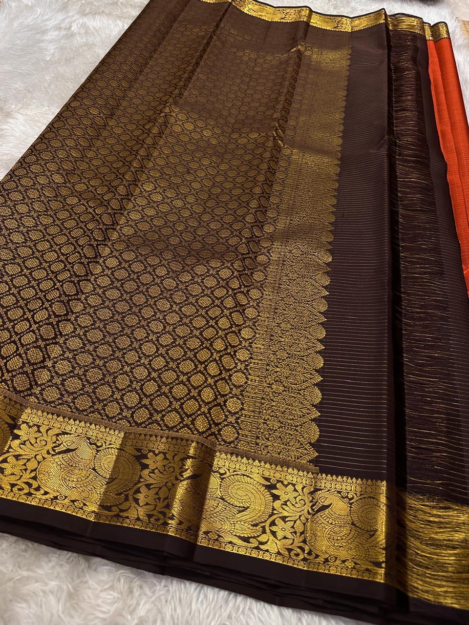 Mantra – Rust brown with coffee brown Kanchipuram Silk Saree with zari Checks with small buttas all over and Antique Peacock zari Border showcasing regal peacocks and floral vines. A richly detailed pallu completes this heritage Zari kattam