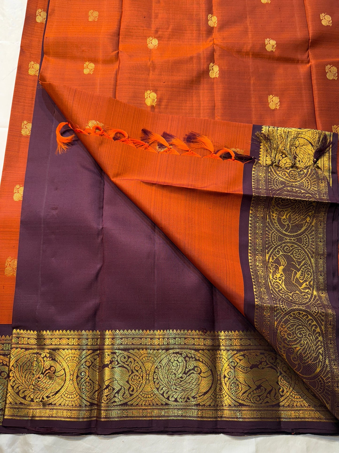 Rust Orange & Wine Korvai – Pure Kanchipuram Silk Saree
Burnt rust-orange shot body with dainty gold paisley buttas
Deep wine korvai borders in antique gold—Annapakshi & Yaali medallions
Grand wine pallu with full-zari jaal & temple panels
Silk Mark