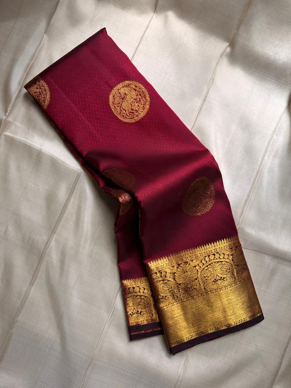 A majestic maroon Kanchipuram silk saree, adorned with intricate golden zari featuring the mythicalYazhi (Yali ) motifs—a symbol of divine strength and protection in Hindu mythology. The grand temple-style gold border adds depth and regality, making this