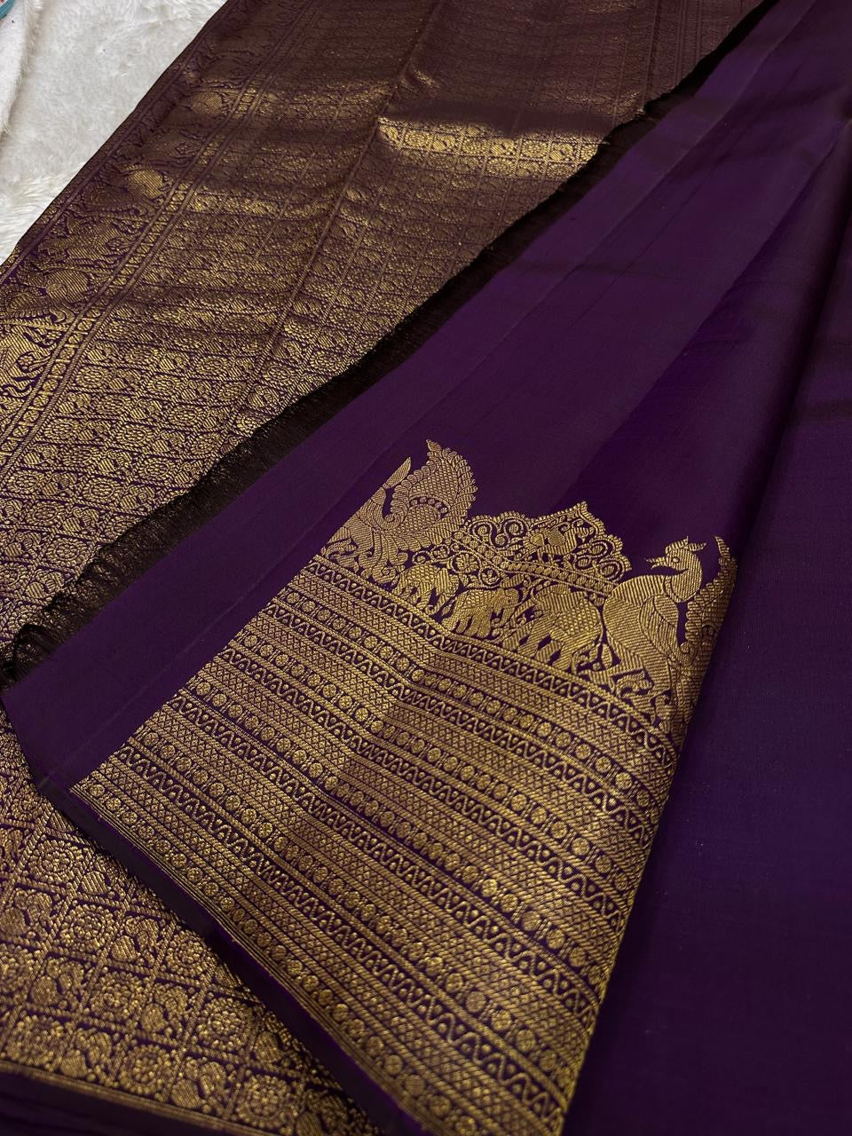 Swarna
Majestic Purple Pure Silk Kanchipuram Saree with Broad Varisaipet Zari Border,Intricately Woven Peacock and Elephant Motifs alongside border . Peacock motifs all over.