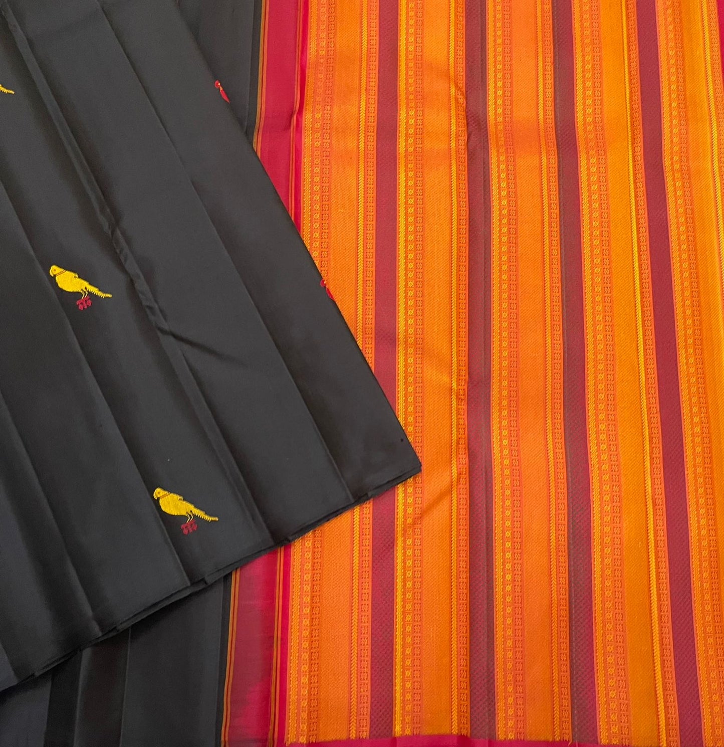 Black Pure Kanchipuram Silk Saree with scattered yellow and red bird motifs laid beside an orange striped pallu with pink border.
