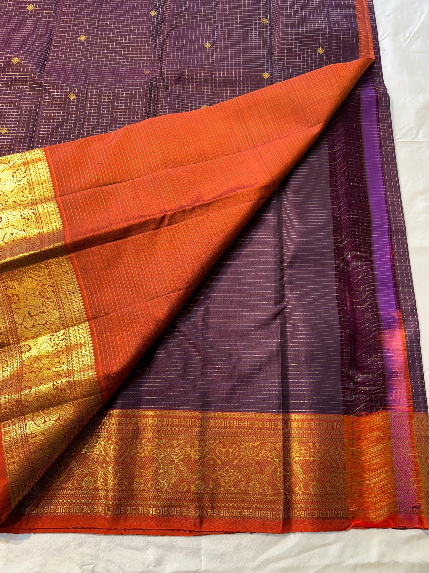 Deep Plum Orange
A regal dance of plum and burnt orange
Micro-checks kissed with golden buttas
Elephant borders marching in heritage grandeur
Brocade pallu glowing in timeless zari brilliance
Silk Mark Certified, delivery in 2 weeks