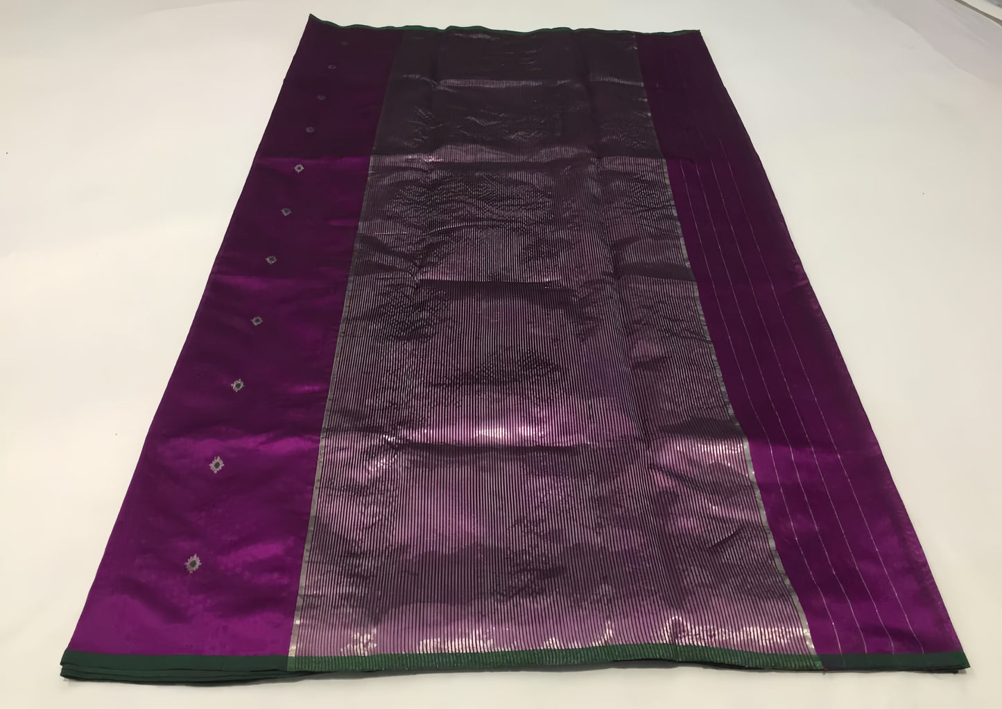 Draped in deep violet and plum, this pure silk Chanderi saree glows with a gentle sheen and graceful vertical zari lines. Delicate diamond meenakari motifs and finely woven borders lend a touch of tradition, with a contrast green selvedge