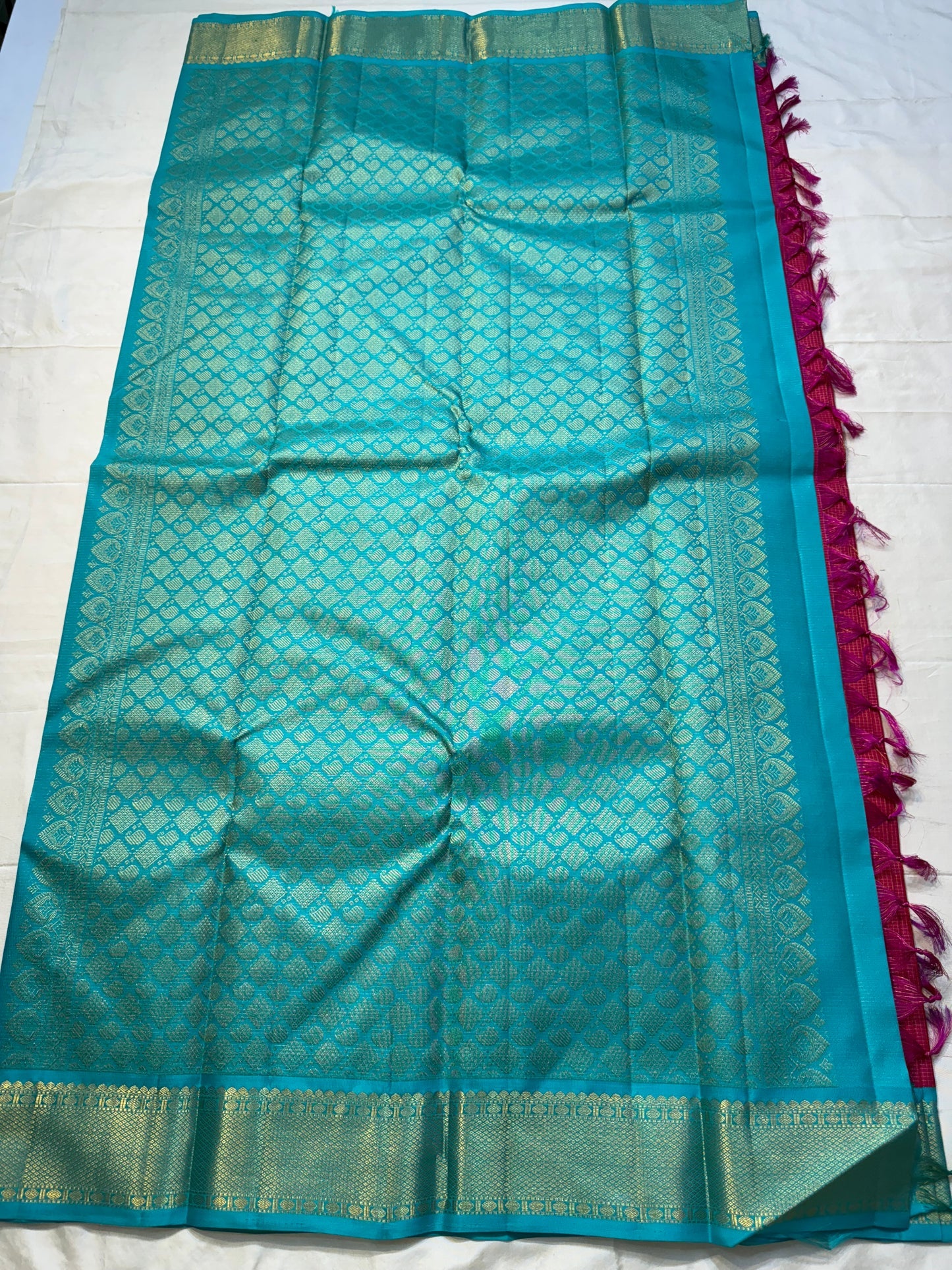 Leela Kattam — Kanchipuram Pure Silk
Rani-pink micro kattam body with soft vaira-oosi sheen
Contrast teal korvai borders with gold lattice & coin roundels
Rich teal pallu with all-over diamond/leaf zari jaal; rani tassels
Silk Mark Certified •