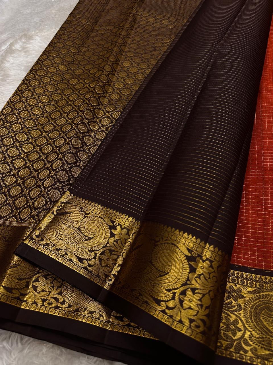 Mantra – Rust brown with coffee brown Kanchipuram Silk Saree with zari Checks with small buttas all over and Antique Peacock zari Border showcasing regal peacocks and floral vines. A richly detailed pallu completes this heritage Zari kattam