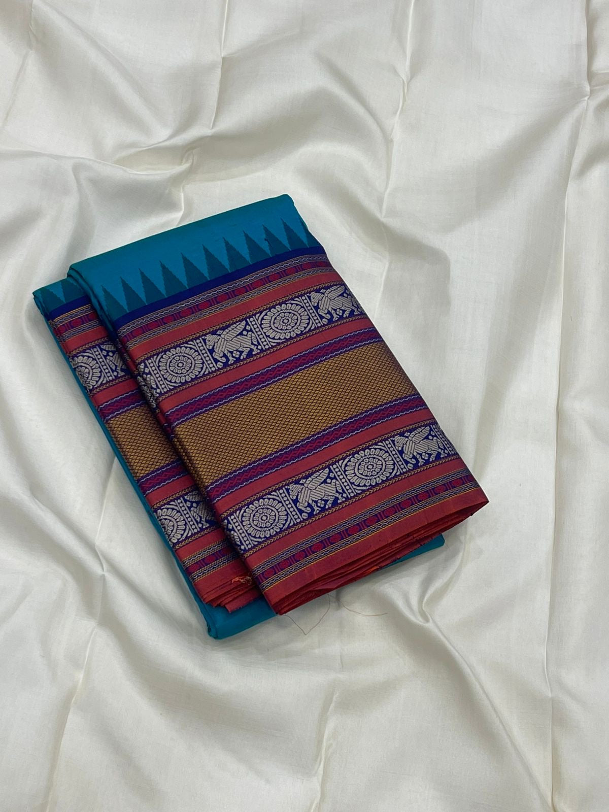 Peacock-teal body with woven silk-thread buttas in navy & coral hues
Korvai contrast ruby-maroon borders with gaja-chakram & temple motifs
Grand varisaipettu striped pallu in navy, mustard & maroon tones
Silk Mark Certified • Ships in Two Weeks