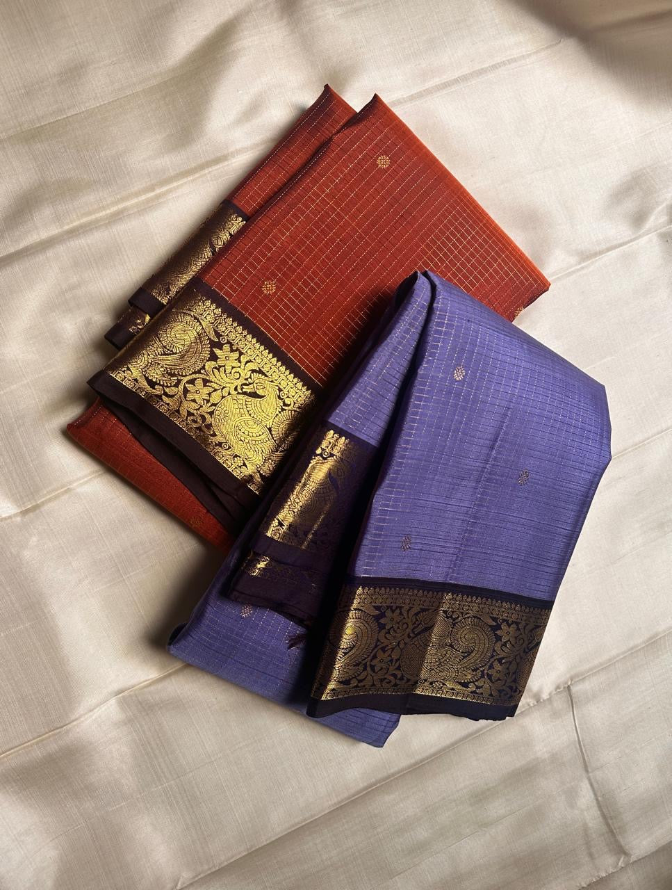 Classic heritage finesse in this lilac blue pure Kanchipuram silk saree Zari kattam , intricately handwoven with fine golden checks across the body. Scattered floral buttas add delicate charm,rich purple peacock border