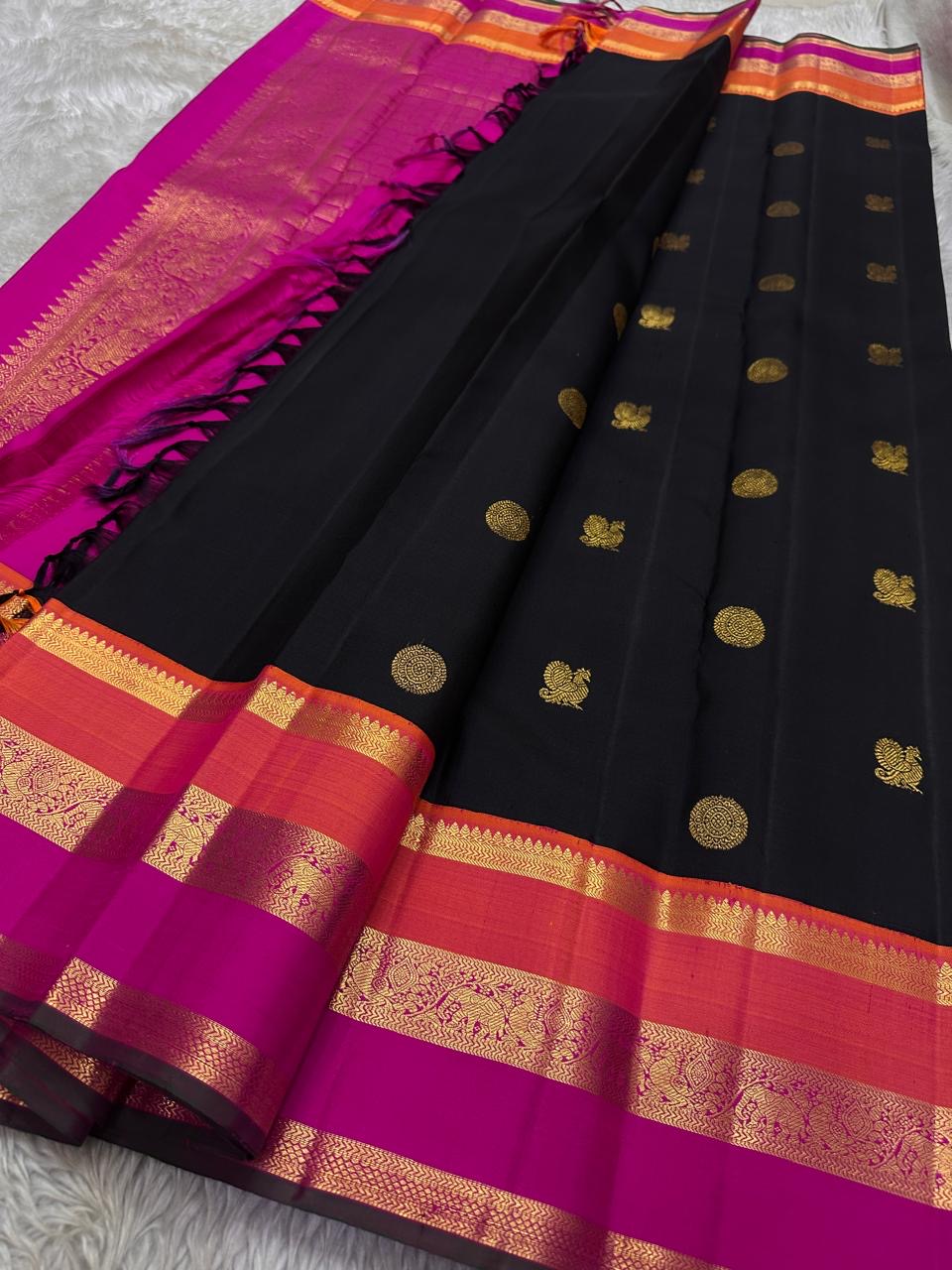 Kanmani — Black & Rani Pure Silk Kanchipuram Saree
Inky black body with gold medallion & peacock buttas
Striking rani-pink and kavi-orange korvai borders with temple-edge zari
Rich rani-pink brocade pallu with grid jaal & heritage vines
Silk Mark Cert