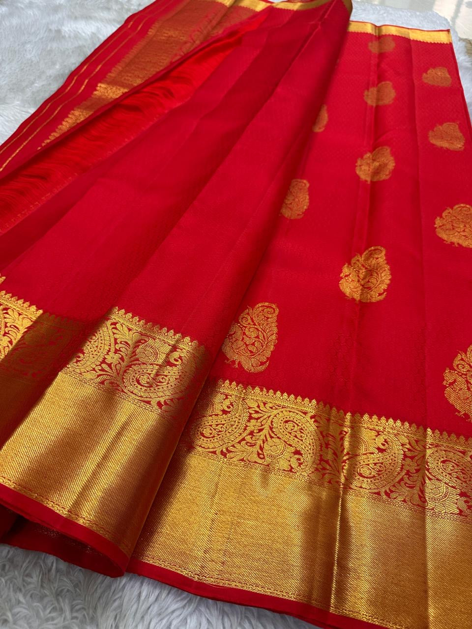 A traditional Kanjivaram (Kanchipuram) silk saree, vibrant red orange peacock floral motifs bavanji border and ornate grid motif Pallu