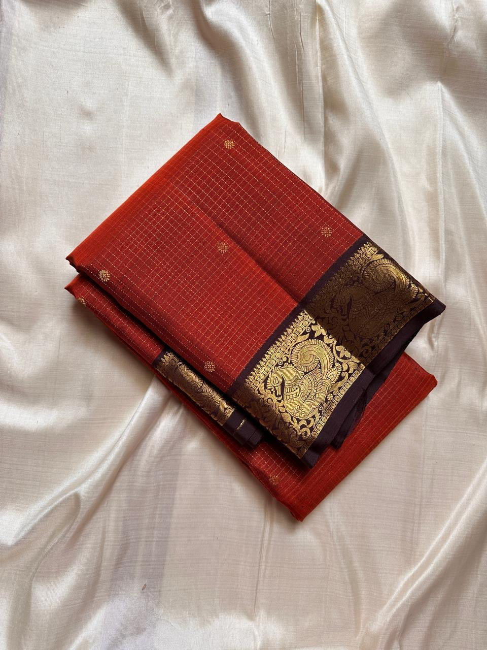 Mantra – Rust brown with coffee brown Kanchipuram Silk Saree with zari Checks with small buttas all over and Antique Peacock zari Border showcasing regal peacocks and floral vines. A richly detailed pallu completes this heritage Zari kattam
