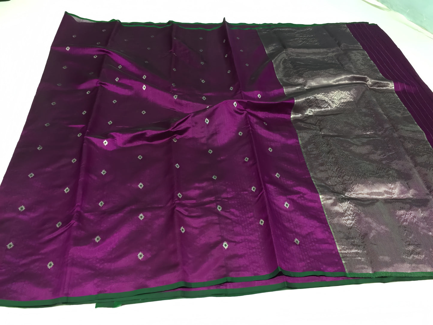 Draped in deep violet and plum, this pure silk Chanderi saree glows with a gentle sheen and graceful vertical zari lines. Delicate diamond meenakari motifs and finely woven borders lend a touch of tradition, with a contrast green selvedge