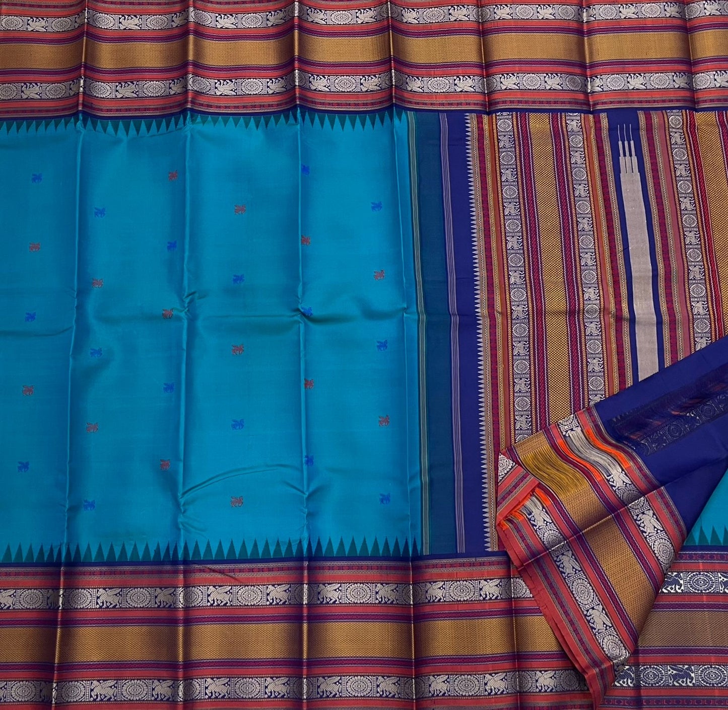 Peacock-teal body with woven silk-thread buttas in navy & coral hues
Korvai contrast ruby-maroon borders with gaja-chakram & temple motifs
Grand varisaipettu striped pallu in navy, mustard & maroon tones
Silk Mark Certified • Ships in Two Weeks