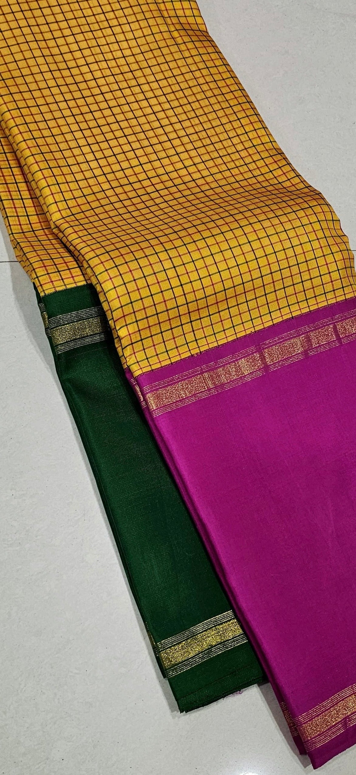 Swarna Kattam Ganga Jamuna — Pure Silk Kanchipuram Saree
Golden mustard kattam checks body • Dual korvai borders in rani pink & emerald green
Rich zari pallu with radiant festive sheen
Contrast emerald blouse with zari selai finish
Silk Mark Certified •
