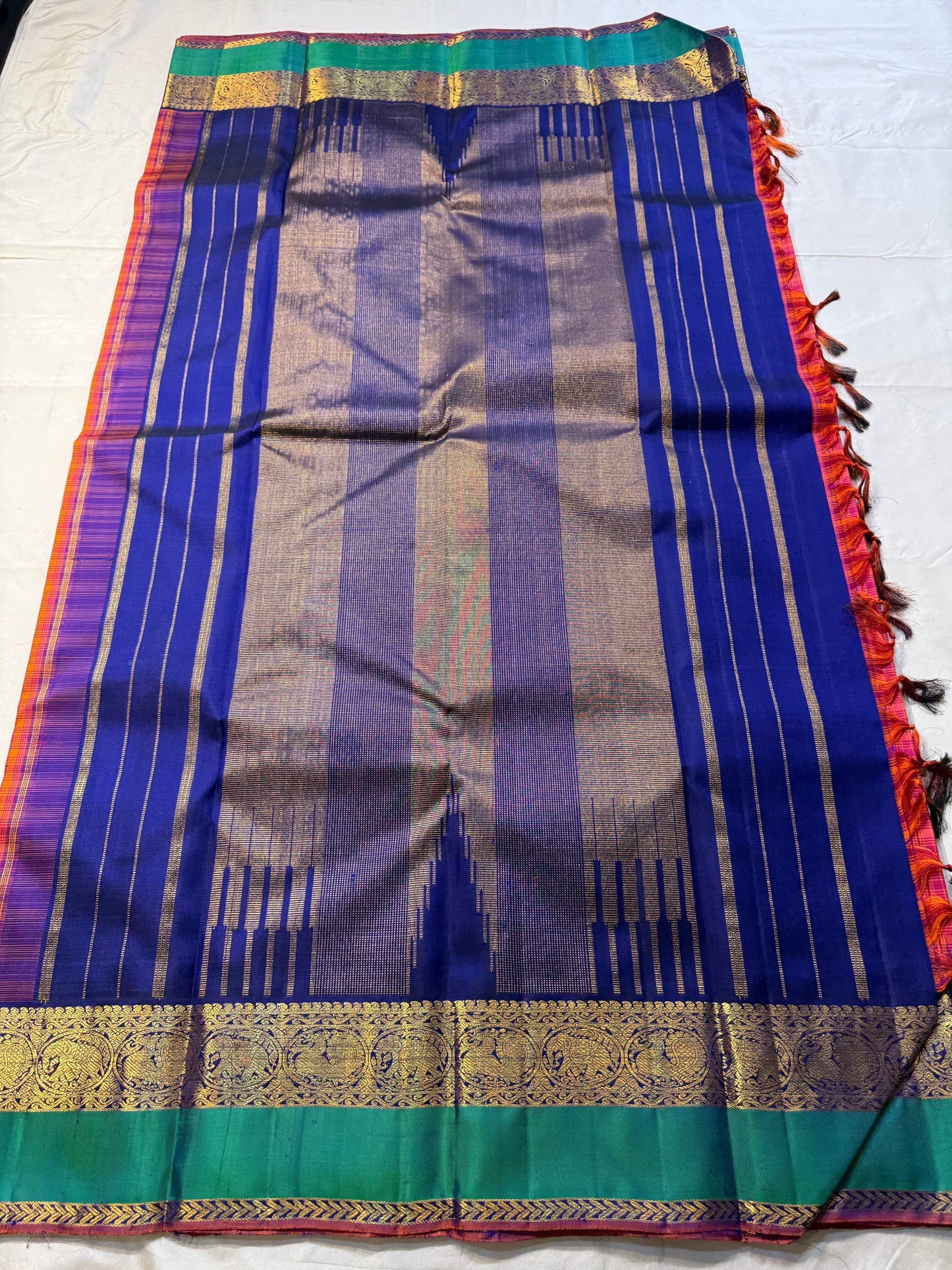 Chemman Maragatha Kattam
Pure Kanchipuram Silk Saree – Reddish-Orange & Maragatha Green Micro Checks
Deep violet korvai borders with gold zari floral motifs
Grand zari pallu with classic brocade detailing
Silk mark certified, ships in 2 weeks