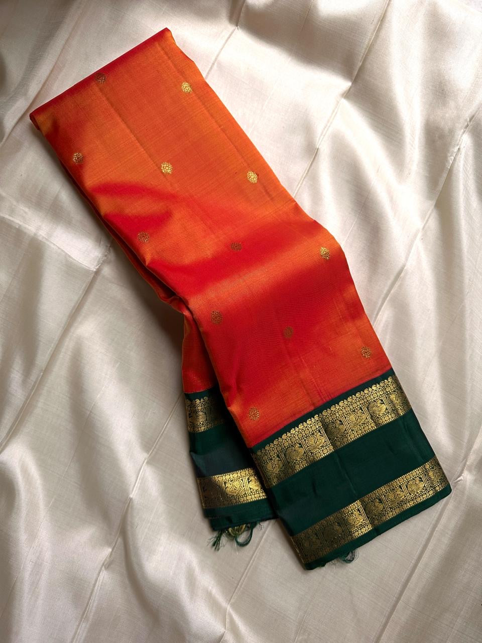 Riya – Orange Silk Saree with Dark Green Zari Border
Radiating warmth and festive charm, Riya glows in a rich ombré of orange and vermilion, adorned with dainty gold butta motifs that shimmer gently with movement.
