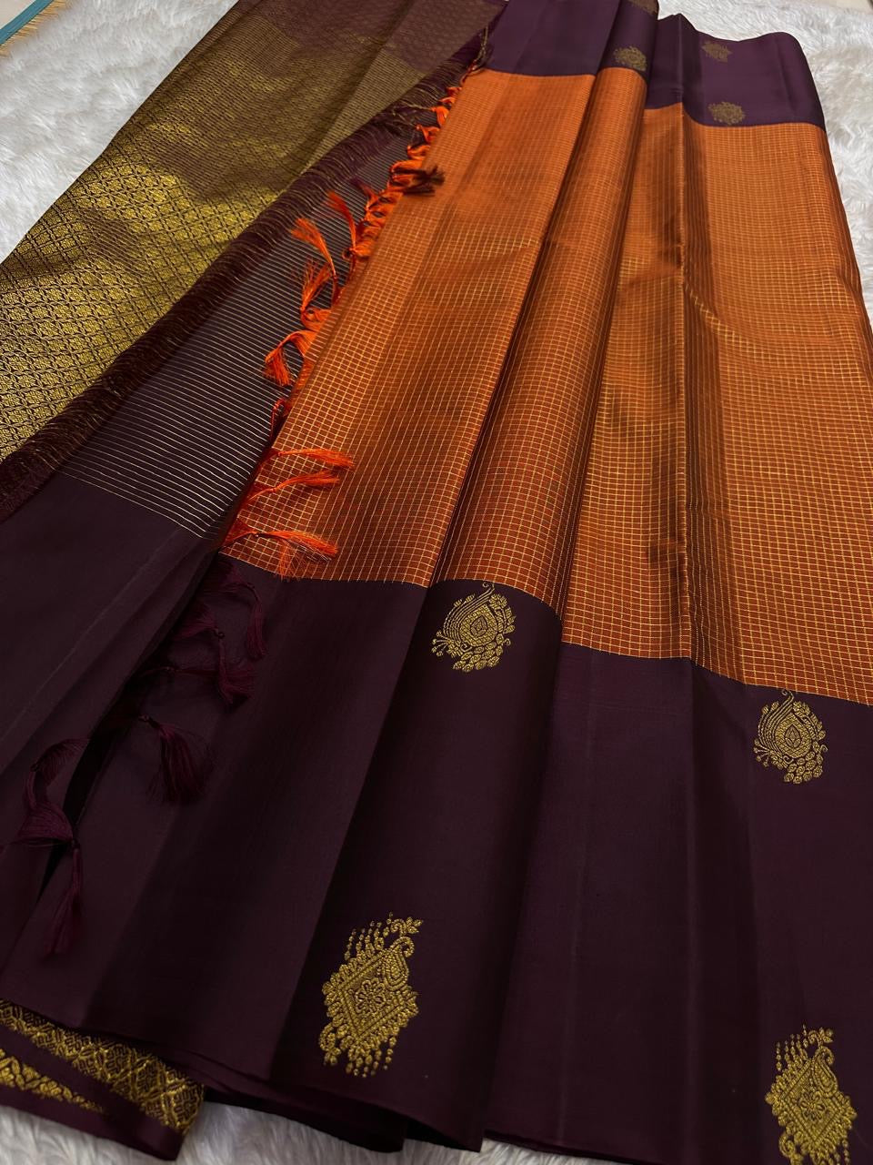 Rust Orange & Wide Broad Silk Korvai – Pure Kanchipuram Silk Saree
Deep wine body adorned with gold ambi buttas for subtle elegance
Contrast rust-orange wide korvai border with podi-kattam micro checks
Grand wine pallu with full-zari diamond jaal